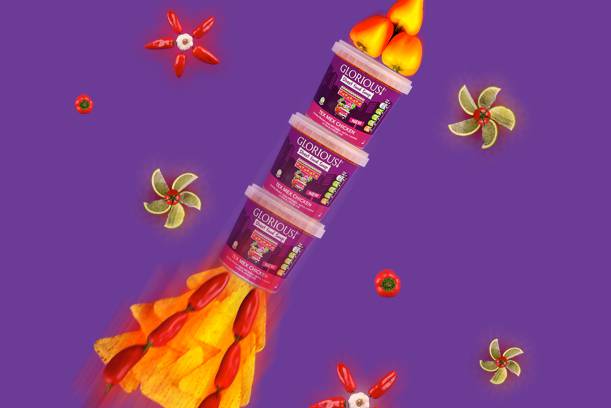 Three stacked containers of Glorious pet food with flames, surrounded by flowers, peppers, and decorative elements on a purple background.