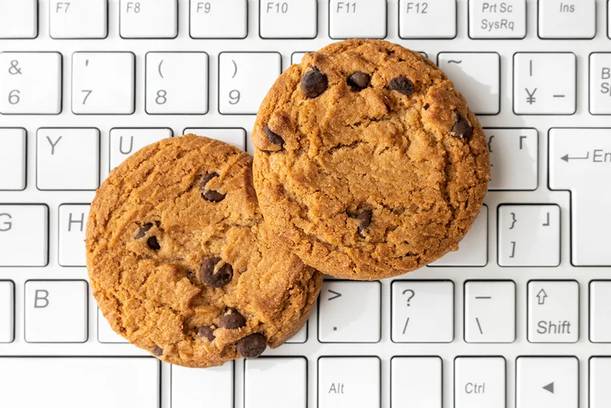 Two chocolate chip cookies resting on a white computer keyboard, with the keys and cookies arranged in a visually balanced composition.