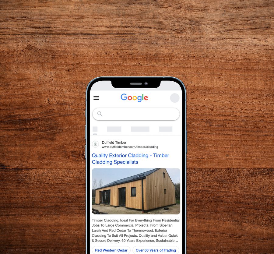 A smartphone displaying a Google search results page for timber cladding, placed on a wooden surface background.