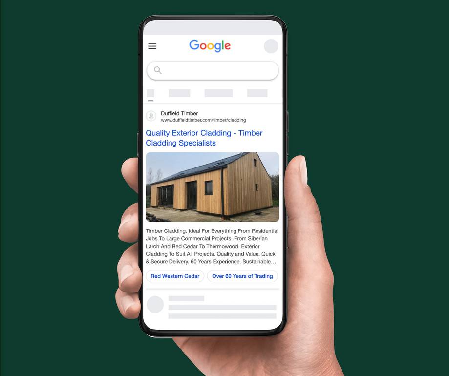 Hand holding a smartphone displaying a Google search result for timber cladding, featuring a wooden building image and blue text about exterior cladding specialists.