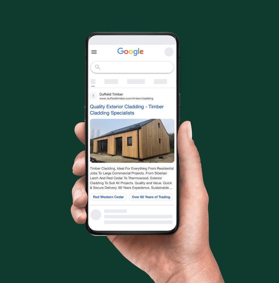 Hand holding a smartphone showing a Google search results page for a timber cladding company, with an image of a wooden building on the screen.