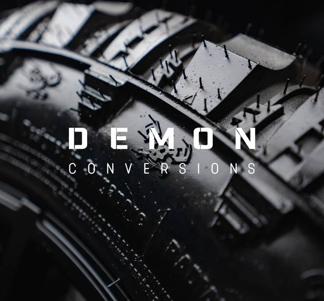 Close-up of a car engine with "DEMON CONVERSIONS" text overlaid in white letters on a dark background.