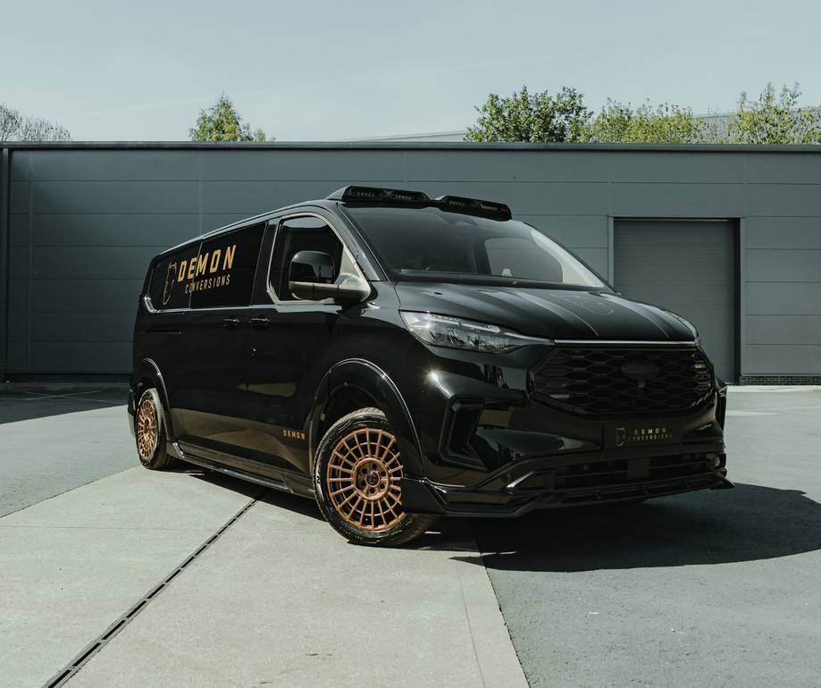Black customised van with gold accents and "Demon Conversions" branding, parked outside a grey industrial building with roof-mounted equipment visible.