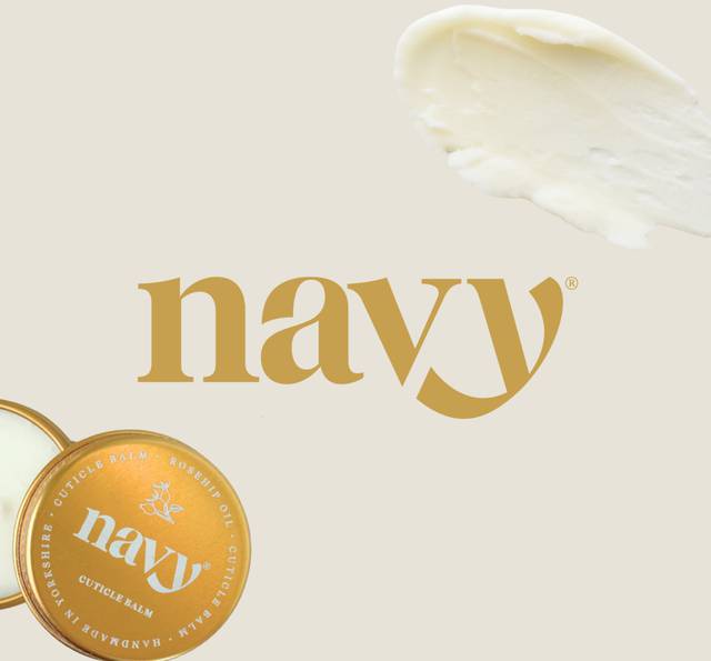 Creamy white balm smear at top right, large gold “navy” logo text in centre, orange round tin at bottom left against pale beige background.