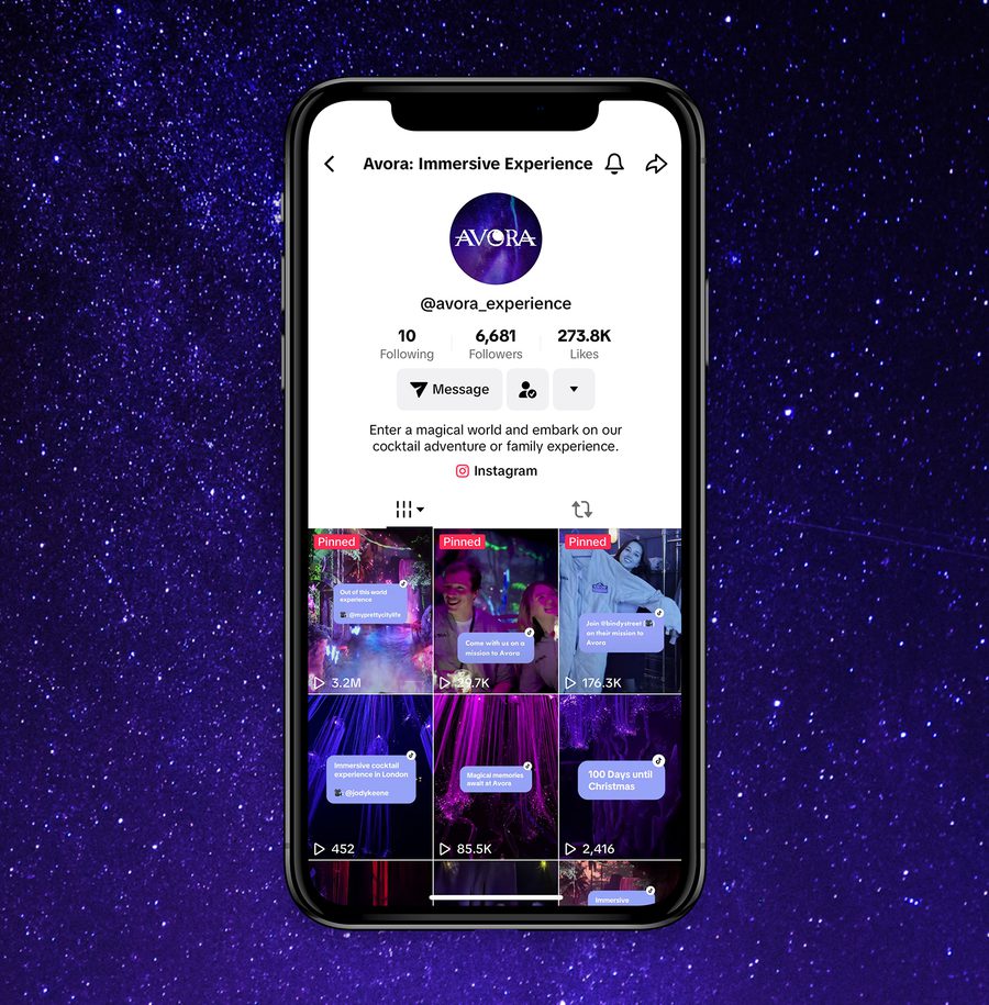 A smartphone displaying a TikTok profile page for Avora: Immersive Experience, with videos about a cocktail adventure and festive events, against a starry purple background.