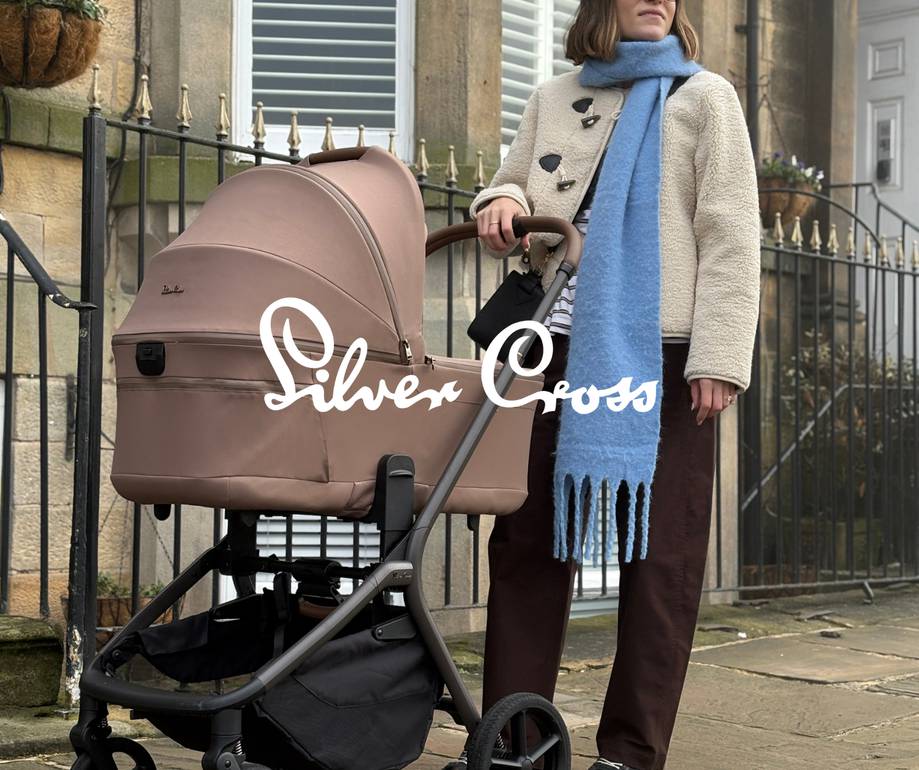 Person in cream coat and blue scarf standing with pink/mauve pram on urban street, Silver Cross branding visible, Georgian architecture background.