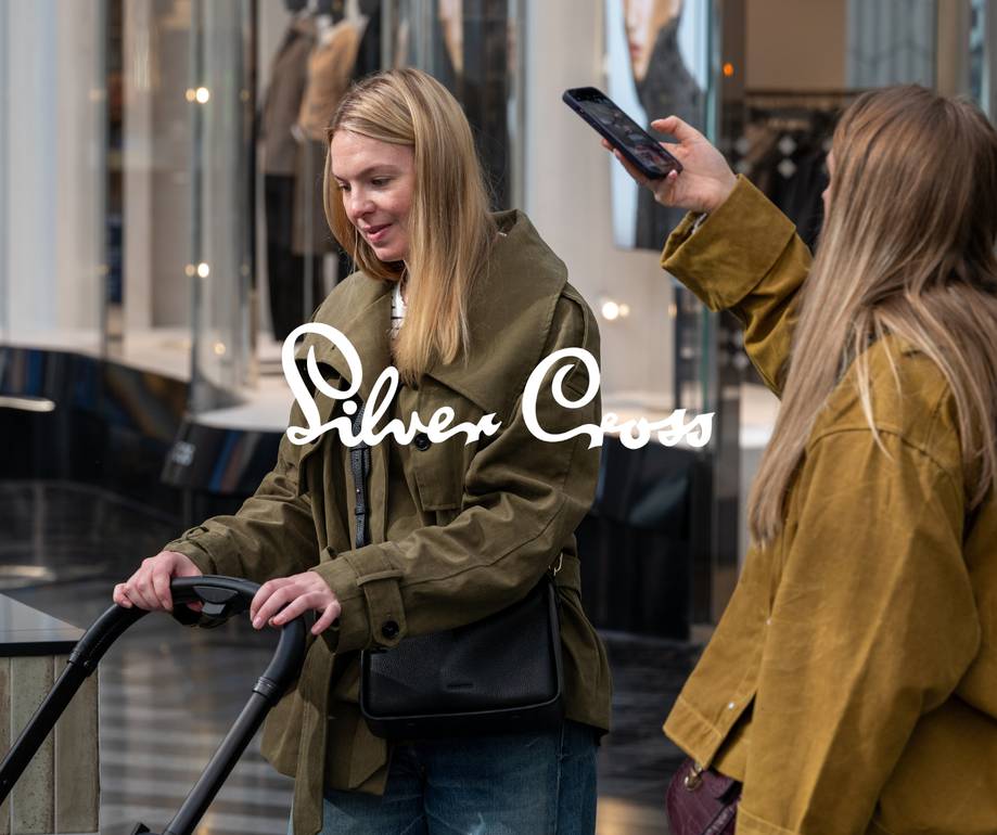 Two people shopping in a mall, one holding an electric scooter and the other taking a photo with a smartphone, with "Silver Cross" text overlay.