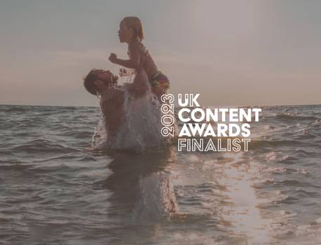 A person holding a child above water during sunset, with text indicating they are a finalist in the 2023 UK Content Awards.