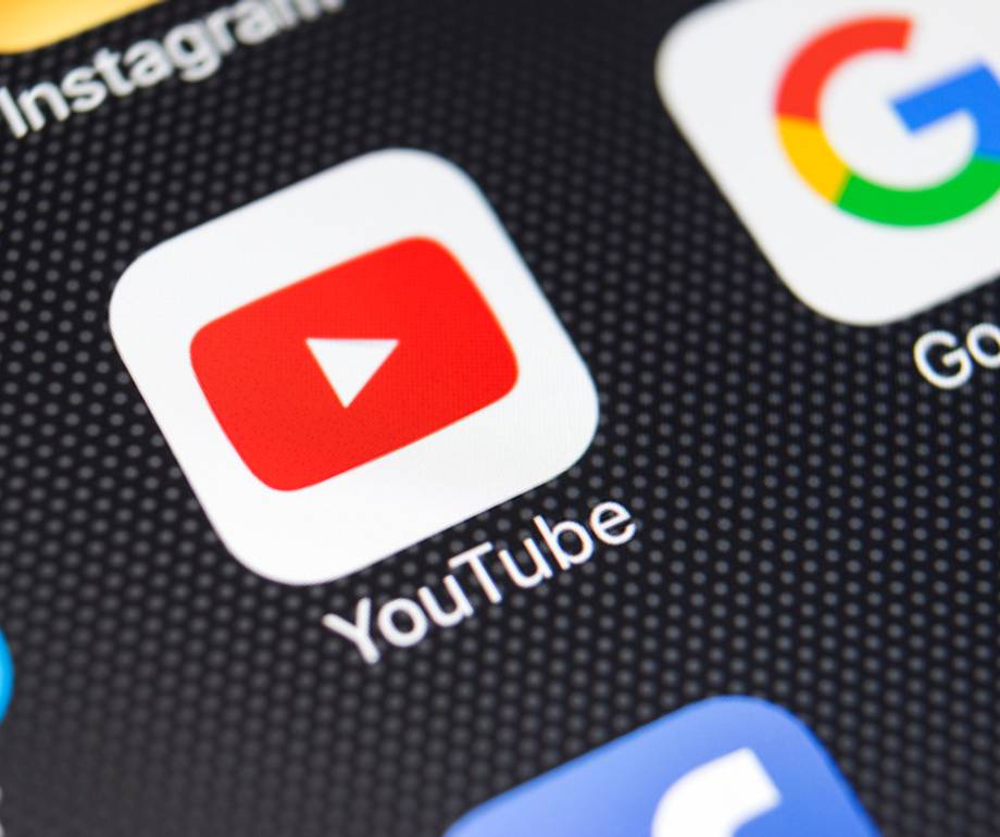 YouTube app icon with a red play button on a smartphone screen, alongside Google app icons, on a dark dotted background.