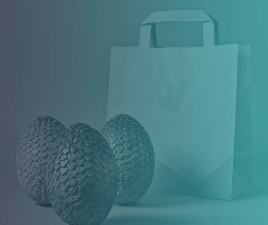 Three textured, dragon-egg-like objects in front of a paper carrier bag printed with the Deliveroo logo, all in a teal monochrome tint.