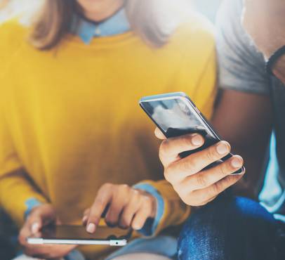 Two people holding smartphones, with one person in a yellow sweater and the other in a grey striped shirt, sitting close together.