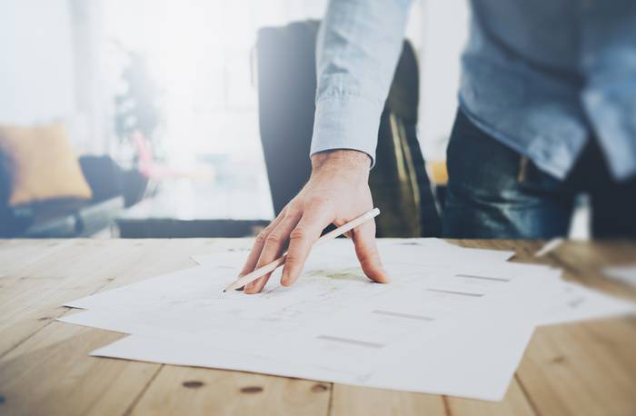 A man with a pen in his hand, leaning over a stack of papers on a wooden desk