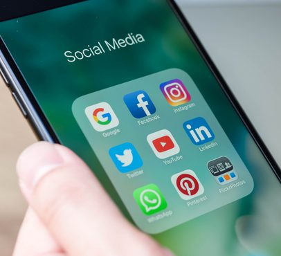 Smartphone screen displaying social media app icons including Google, Facebook, Instagram, Twitter, YouTube, LinkedIn, Pinterest, WhatsApp, and FlickrPhotos.