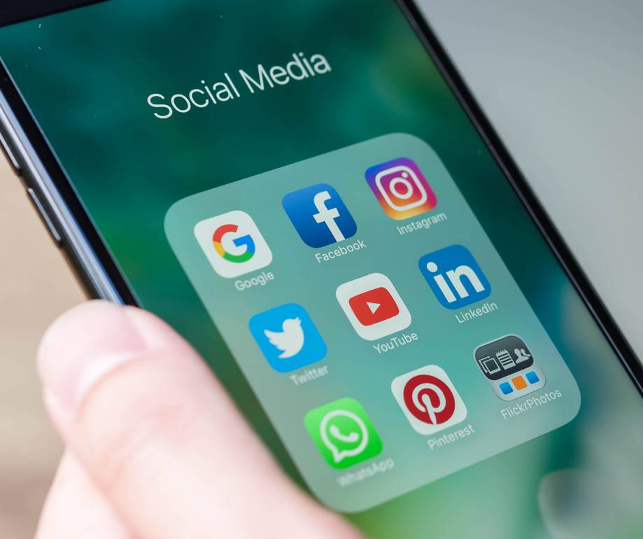 Smartphone screen displaying social media app icons including Google, Facebook, Instagram, Twitter, YouTube, LinkedIn, Pinterest, WhatsApp, and FlickrPhotos.