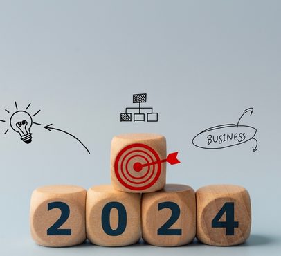 Wooden blocks display the year 2024 with the '0' block featuring a red target icon, surrounded by sketches of a lightbulb, organisational chart, and "Business".