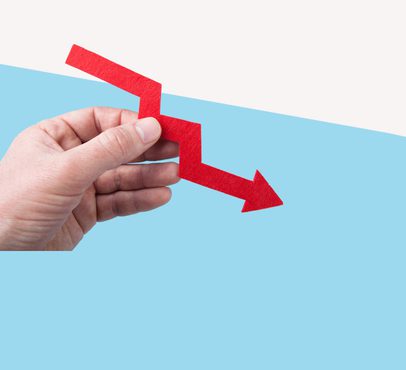 A hand holding a red downward arrow with a zigzag shape, representing decline or decrease against a split light blue and white background.