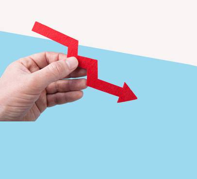 A hand holding a red downward arrow with a zigzag shape, representing decline or decrease against a split light blue and white background.