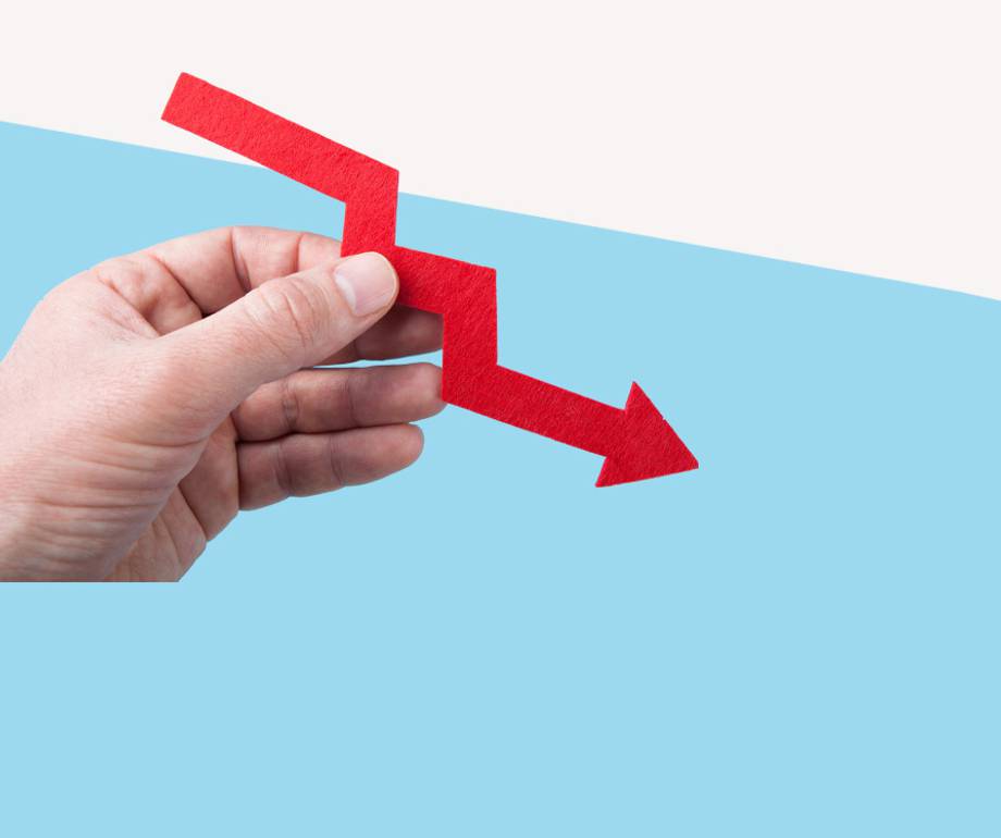 A hand holding a red downward arrow with a zigzag shape, representing decline or decrease against a split light blue and white background.