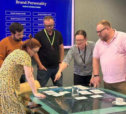 Participants in a brand strategy workshop discussing and selecting attributes, with a "Brand Personality" screen in the background.