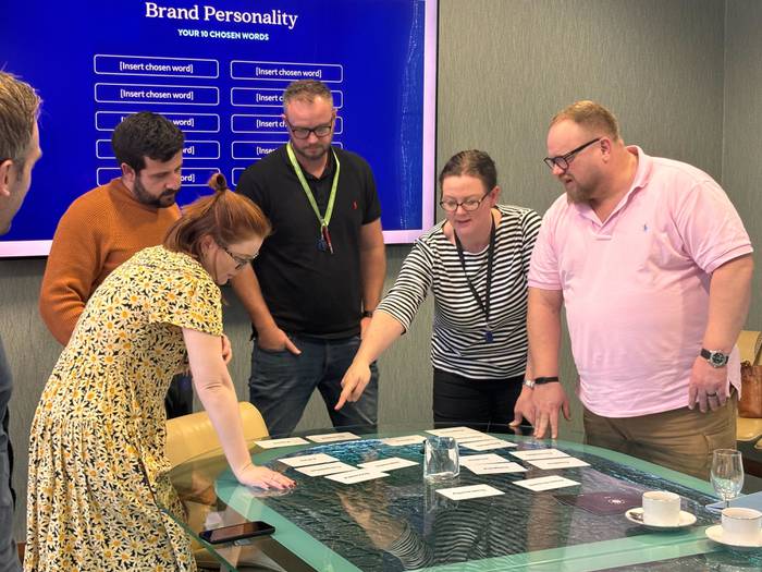Participants in a brand strategy workshop discussing and selecting attributes, with a "Brand Personality" screen in the background.