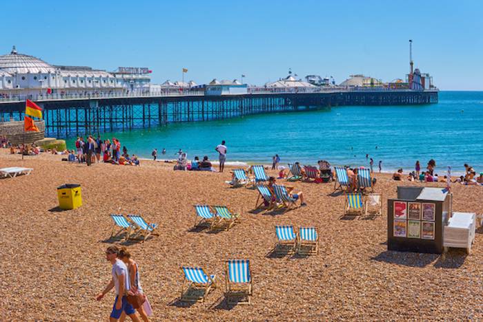 A sunny beach, with lots of people sat sunbathing and playing in the sea.