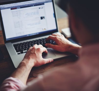Person using a laptop at a wooden desk, viewing a social media profile or webpage on the screen.