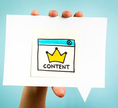 Hand holding a paper with a colourful illustration of a web browser window showing a yellow crown and the word "CONTENT".