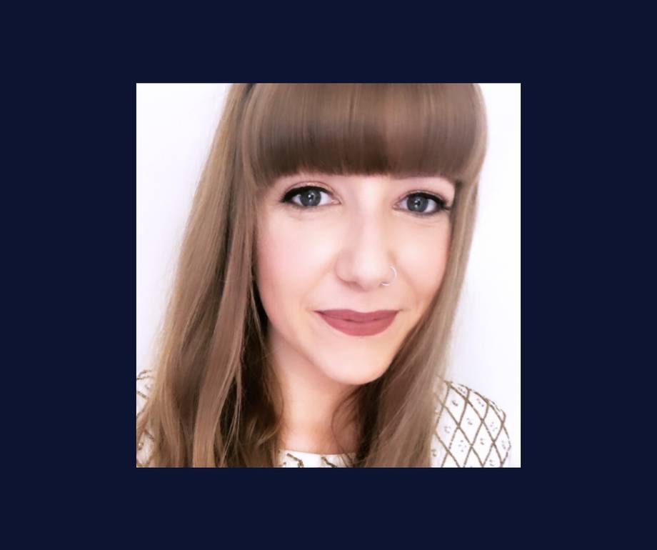 A woman with straight, light brown hair and full bangs, smiling slightly, wearing makeup and a white top with a diamond pattern.