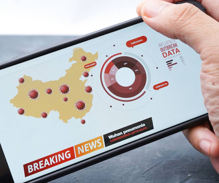 A hand holding a smartphone displaying a map of China with red virus icons, a circular chart, and news headline about Wuhan pneumonia and outbreak data.