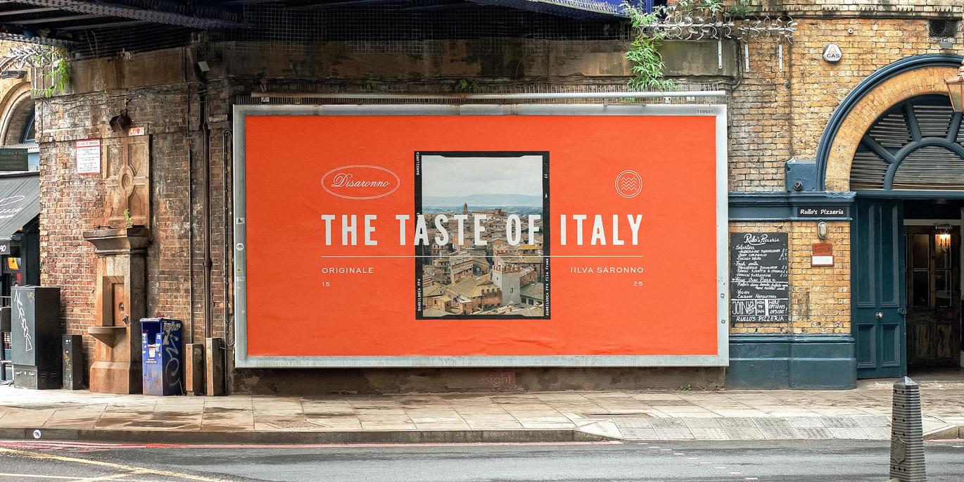 An image of a billboard advert featuring a bright orange poster with the new Disaronno font overlaid onto it and a picture of the Italian countryside in the middle. The text says The Taste of Italy - Disaronno's tag line.