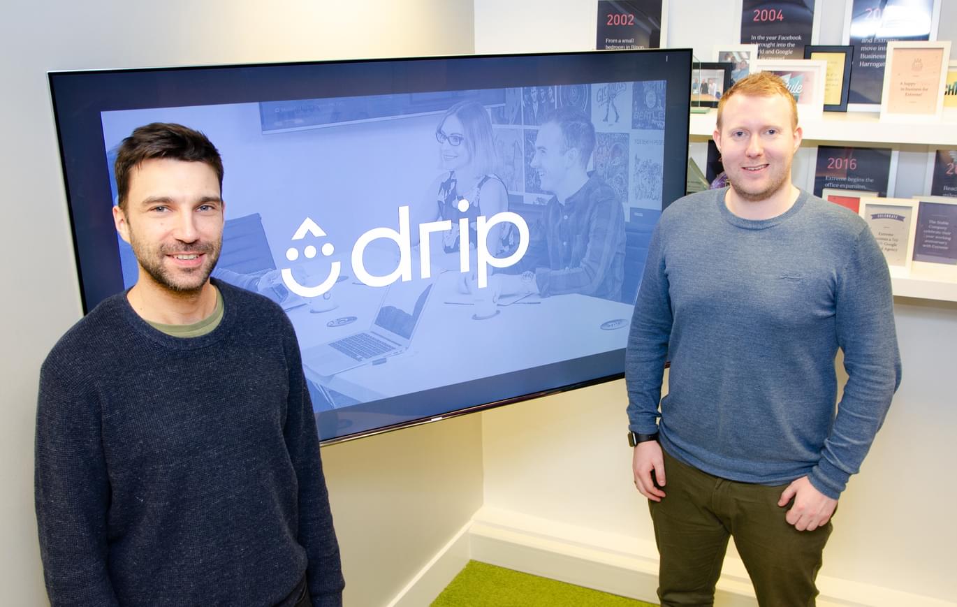 Two men stood in front of the Drip logo on a TV screen.