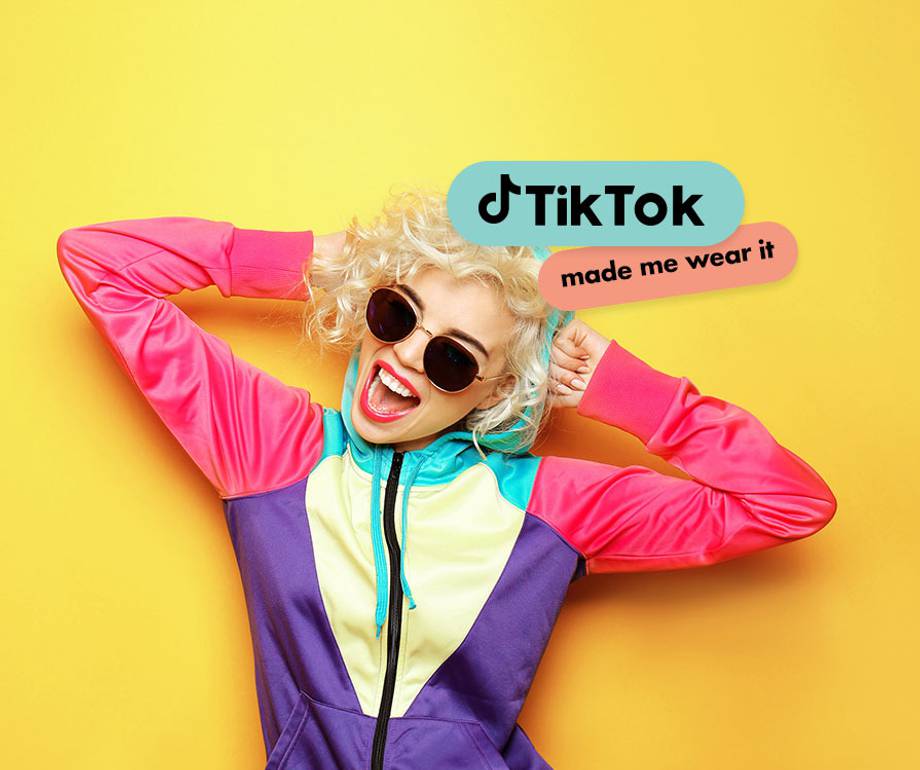 Woman with curly blonde hair, wearing colourful jacket and sunglasses, smiling against yellow background with TikTok and made me wear it stickers.