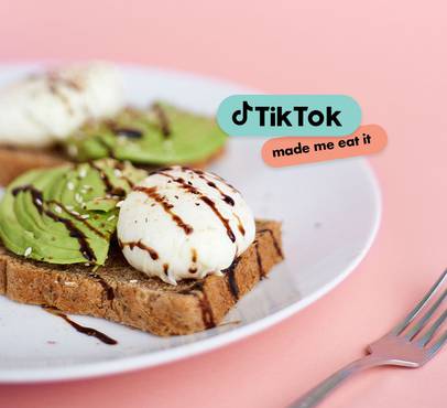 A plate of toast topped with sliced avocado, a poached egg drizzled with chocolate, on a pink background with TikTok and "made me eat it" text overlays.
