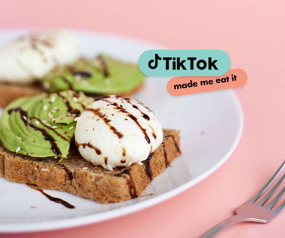 A plate of toast topped with sliced avocado, a poached egg drizzled with chocolate, on a pink background with TikTok and "made me eat it" text overlays.