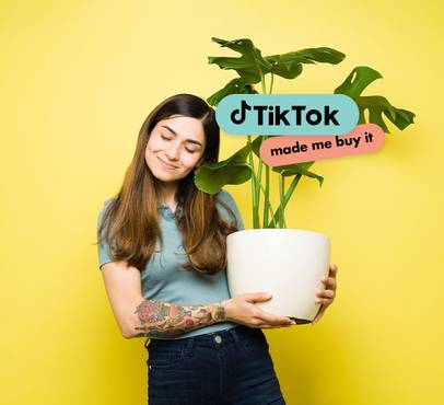 Smiling person with long brown hair and closed eyes holds a white pot with a monstera plant against yellow; TikTok "made me buy it" overlay.