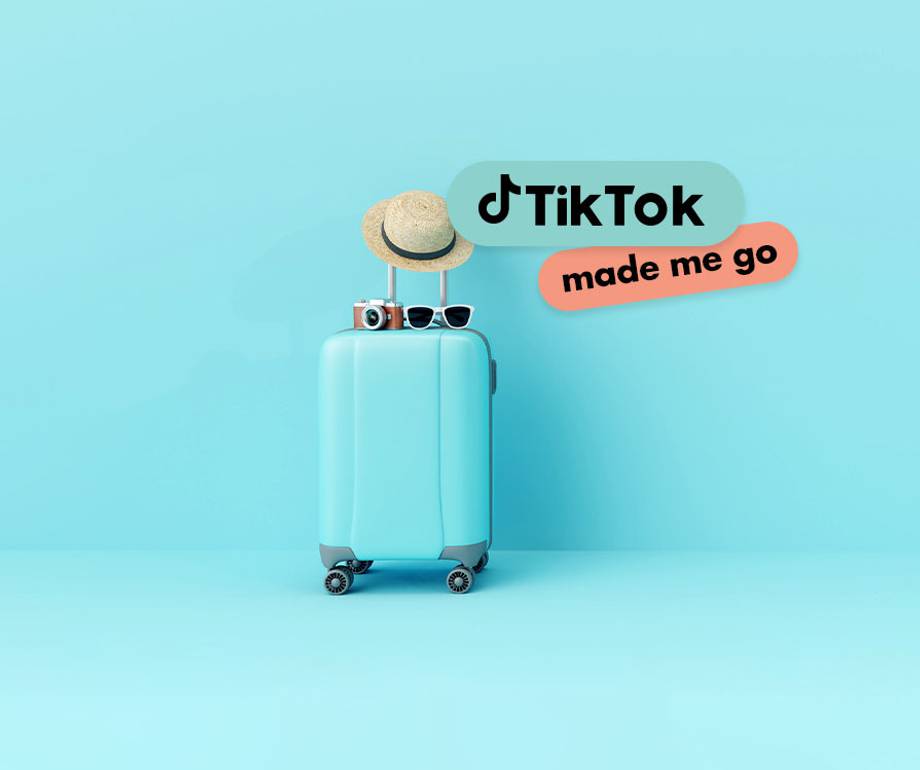 A light blue suitcase with a straw hat, sunglasses, and a camera on top, with TikTok logo and "made me go" text bubbles against a matching blue background.