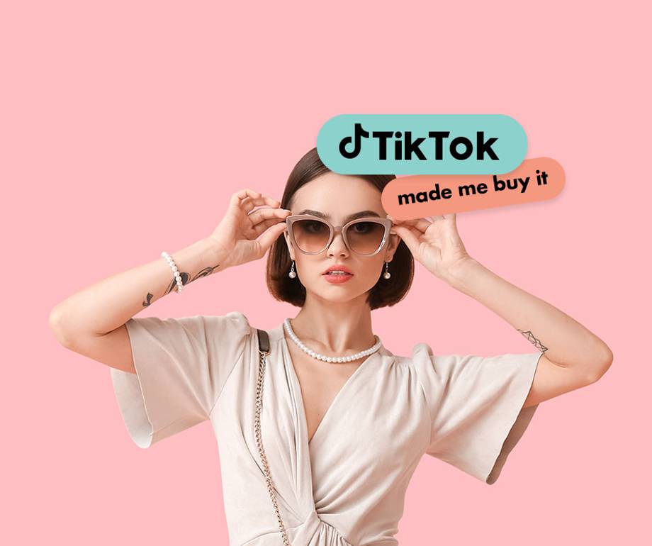 Person with a bob haircut, clear sunglasses and a pearl necklace in a cream wrap dress on a pink background, beside teal TikTok and coral made me buy it labels