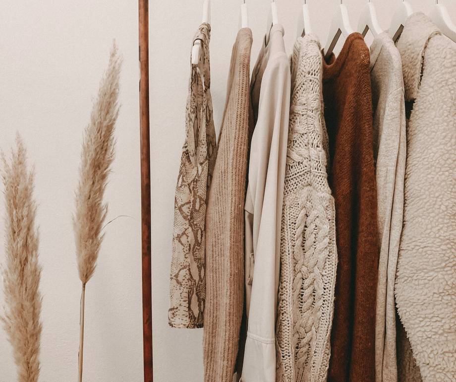 A row of beige and brown textured and knitted sweaters hanging on a white clothing rack with a minimal background.