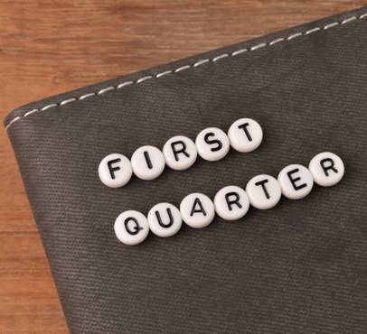 Scrabble tiles spelling "FIRST QUARTER" on a dark textured surface with a wooden background.