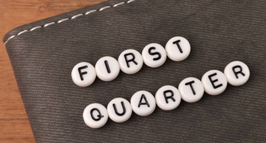 Scrabble tiles spelling "FIRST QUARTER" on a dark textured surface with a wooden background.