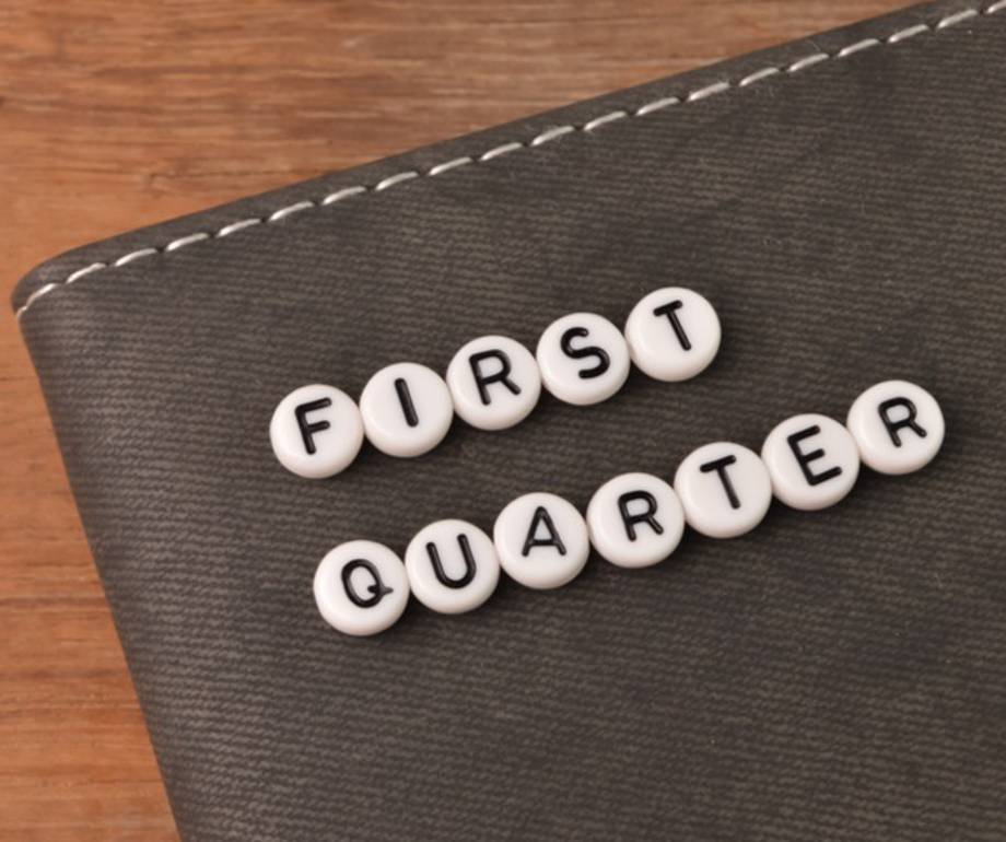 Scrabble tiles spelling "FIRST QUARTER" on a dark textured surface with a wooden background.