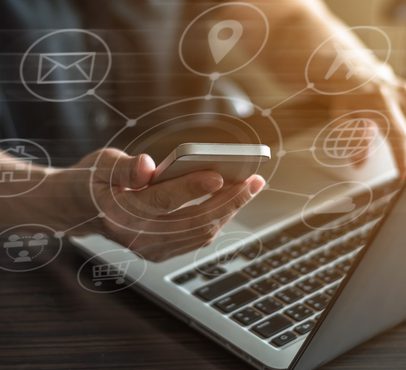 Person holding a smartphone above a laptop with digital network icons overlaying the image.