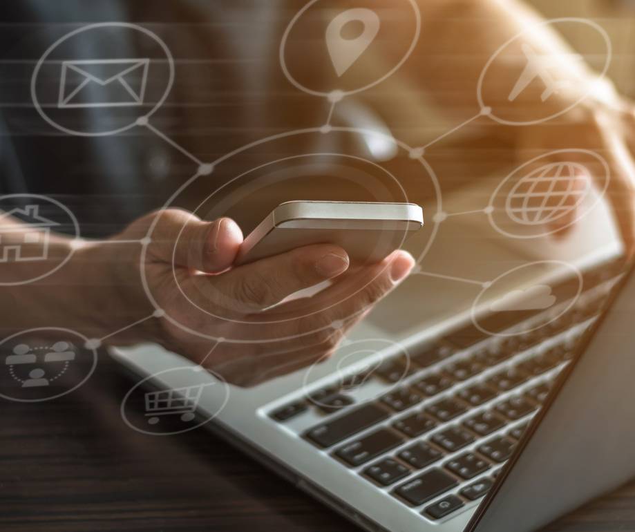 Person holding a smartphone above a laptop with digital network icons overlaying the image.