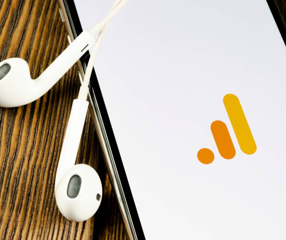 Smartphone with a white screen displaying a logo in shades of orange, accompanied by white earphones on a wooden surface.