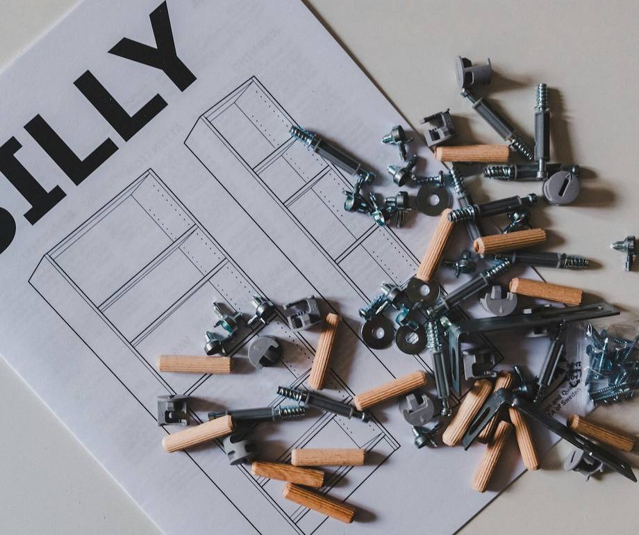 A white instruction sheet printed with "BILLY" and line drawings of a bookcase, partly covered by wooden dowels, grey cam locks, metal screws and fittings spilling from a small clear bag.