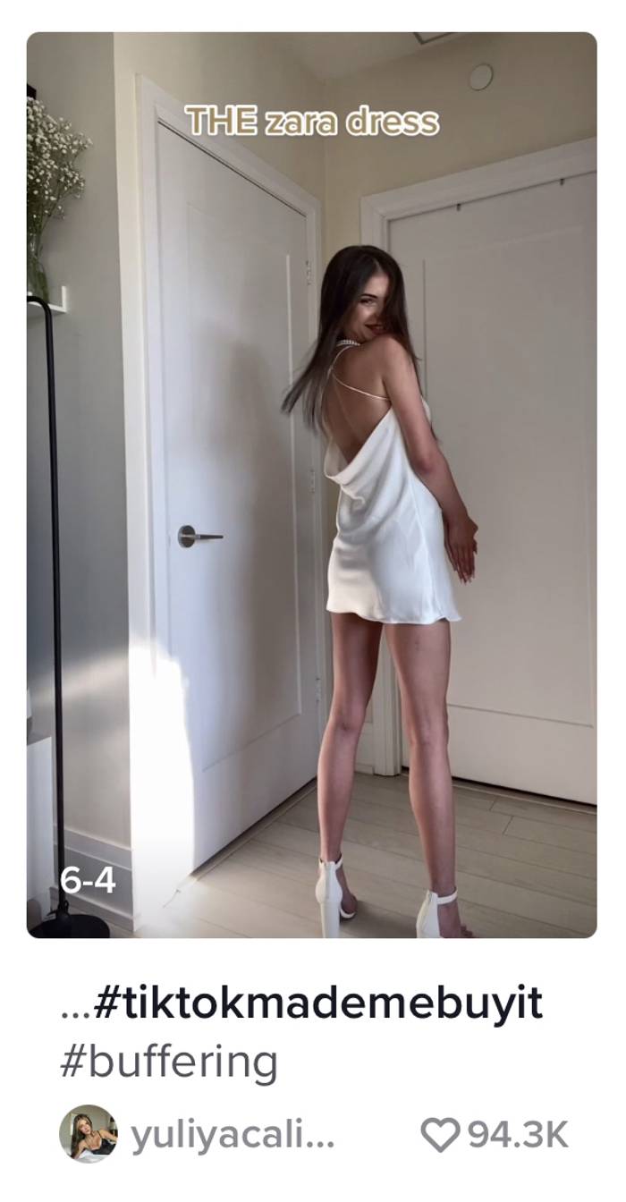 A screenshot of a woman wearing a cream, silk dress.