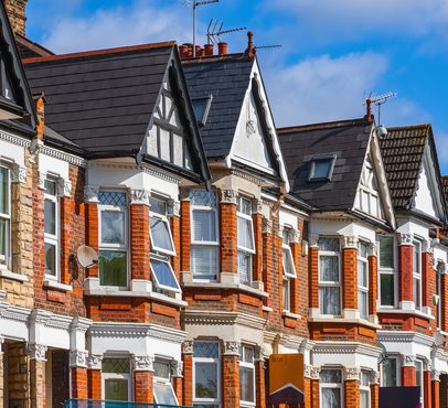 Row of ornate Victorian houses with red brick and white trim under a blue sky, showcasing varied rooftop designs and a "To Let" sign.