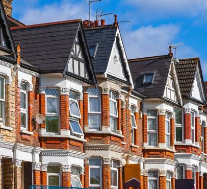 Row of ornate Victorian houses with red brick and white trim under a blue sky, showcasing varied rooftop designs and a "To Let" sign.