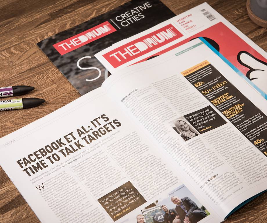 An open newspaper on a wooden table with an article titled "Facebook et al: It’s time to talk targets", surrounded by three pens and a magazine in the background.