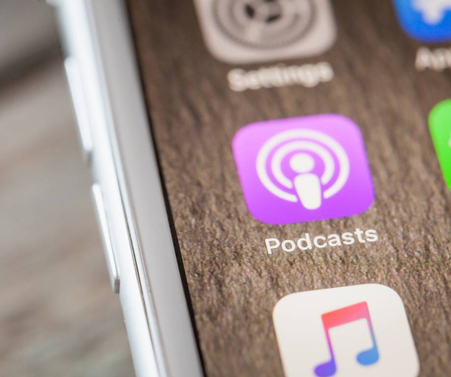 Close-up of an iPhone screen showing the Podcasts app icon on a textured wooden background.